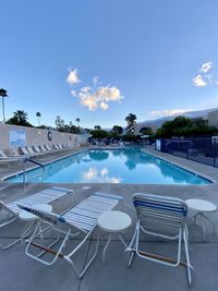 Empty chairs by swimming pool against sky