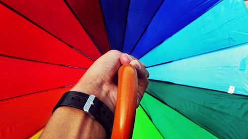 Cropped hand of man holding multi colored umbrella