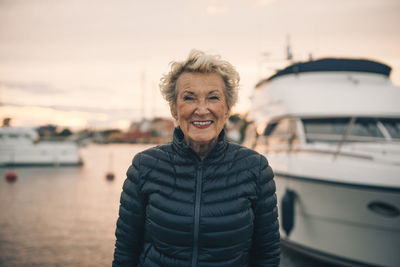 Portrait of happy senior woman standing at harbor during sunset