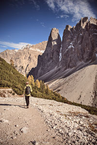 Rear view of man walking on road by mountains against sky