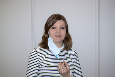 Portrait of smiling woman wearing mask standing against wall