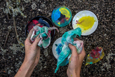 Close-up of hand holding multi colored tissue and colors, painting in the back