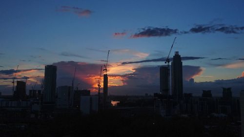 Silhouette of city against cloudy sky during sunset