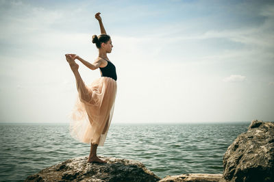 Young woman doing yoga at beach against sky