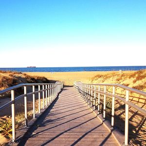 Empty footpath leading towards sea against clear sky