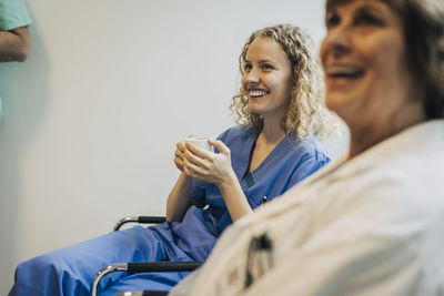 Happy female nurse holding coffee cup while sitting on chair by colleague