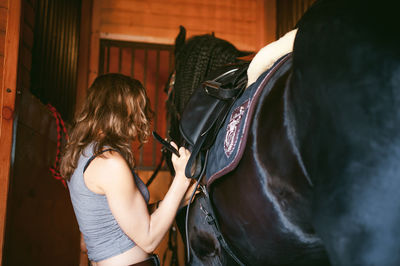 Side view of young woman adjusting horse bridle at stable