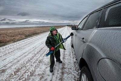 Boy cleaning snow covered car on road