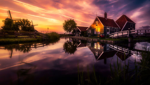Scenic view of river by buildings against sky at sunset