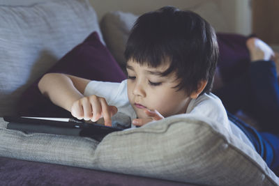 Boy using digital tablet while lying on sofa at home