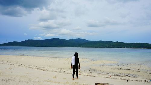 Rear view of woman walking at beach against sky