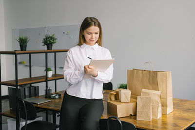 A cute girl makes notes in a notebook next to eco packages on the table