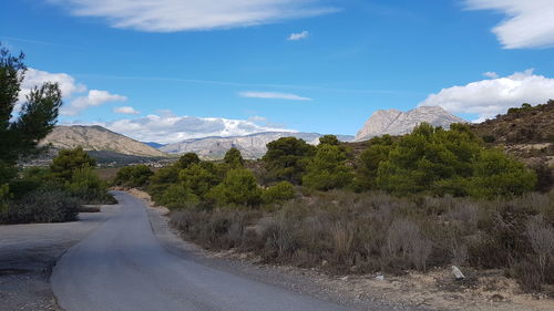 Road amidst trees and mountains against sky