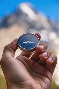 Hand of an anonymous person holding a small round compass near a picturesque mountain valley