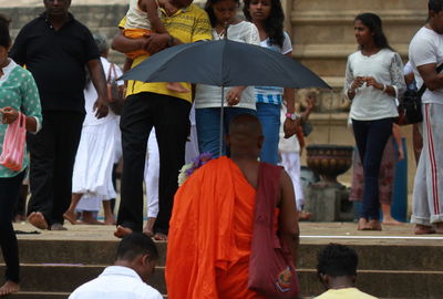 Monk with umbrella amidst people on steps