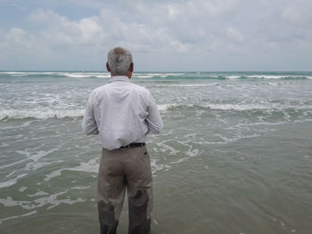 Rear view of man standing on shore at beach against sky