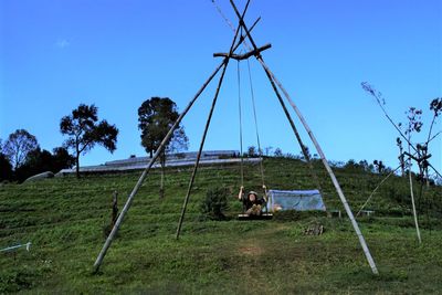 Woman swinging on grassy hill against sky