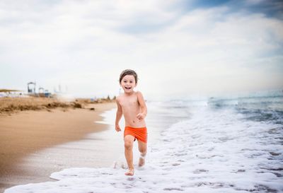 Full length portrait of shirtless boy running on beach