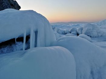 Snow covered landscape against sky during sunset