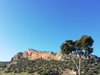 Low angle view of rocky mountain against clear blue sky