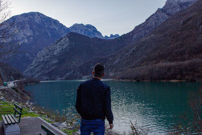 Rear view of man looking at lake against mountain range