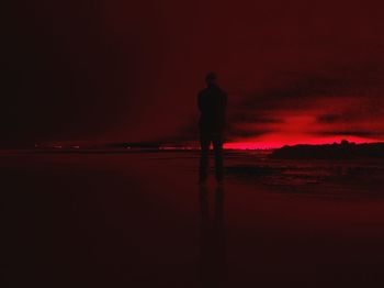 Silhouette man standing in sea against sky during sunset