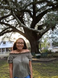 Portrait of smiling young woman standing against trees