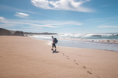 Rear view of woman walking at beach against sky