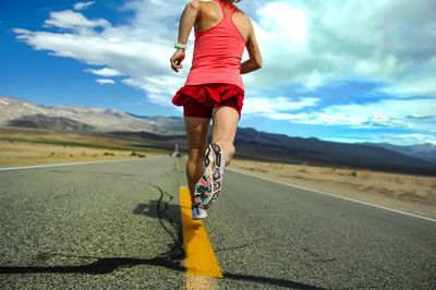 Low section of woman running on road against sky