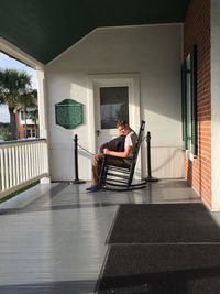 Side view of brothers sitting on rocking chair against house