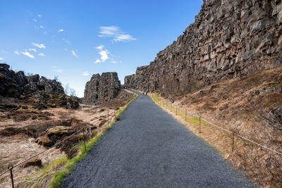 Road amidst rock formations on cliffs against sky at thingvellir national park