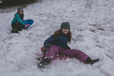 Full length of girls sitting on bobsled in snow