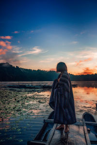 Woman standing on boat at lake against sky during sunset