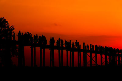 Silhouette people walking on wooden bridge during sunset