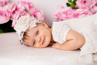 Baby girl lying on her stomach and smiles on the bed in clothes and a pink headband