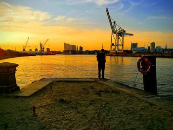 Rear view of man standing at commercial dock during sunset