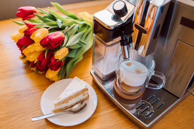 Cup of coffee with milk, piece of cake and tulips flowers on wooden kitchen table. freshly brewed 