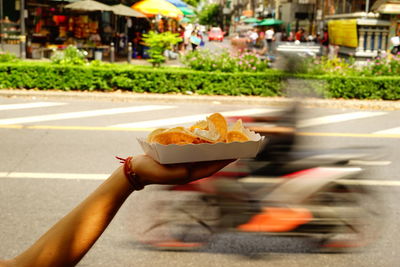 Close-up of hand holding nacho chips in plate against blurred motorcycle