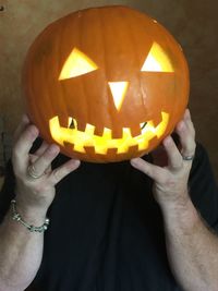 Midsection of person holding pumpkin against illuminated halloween