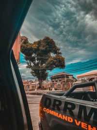 Road sign by trees against sky seen through car windshield