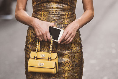 Midsection of woman holding mobile phone while standing on road