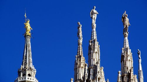 Statues on spires of milan cathedral against clear blue sky