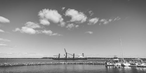 Cranes and boats at commercial dock in sea against sky