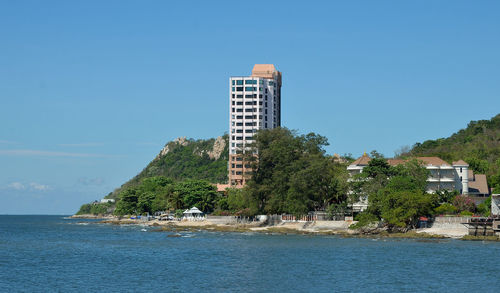 Buildings by sea against clear blue sky