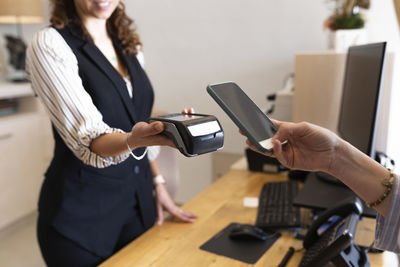 Businesswoman holding mobile phone by credit card reader at hotel reception