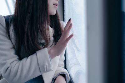 Midsection of woman sitting by glass window in train