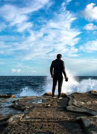 Rear view of man standing on shore against sky