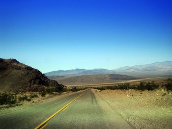 Empty road along landscape and mountains against blue sky