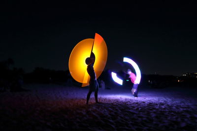 People with illuminated lights against sky at night