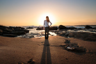 Silhouette of woman standing on beach at sunset